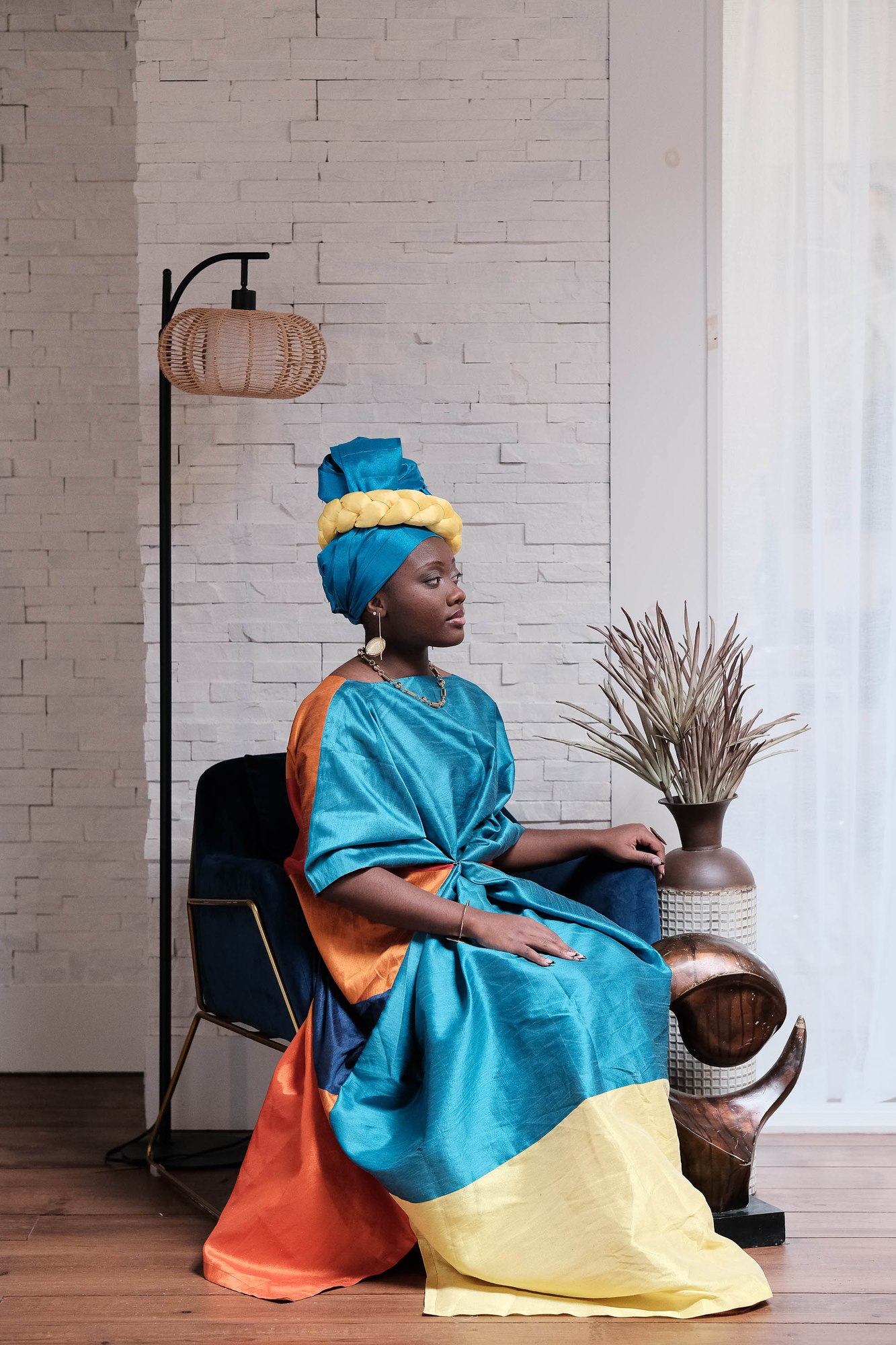 Marie-Paul seated in a teal headwrap and flowing teal and orange gown