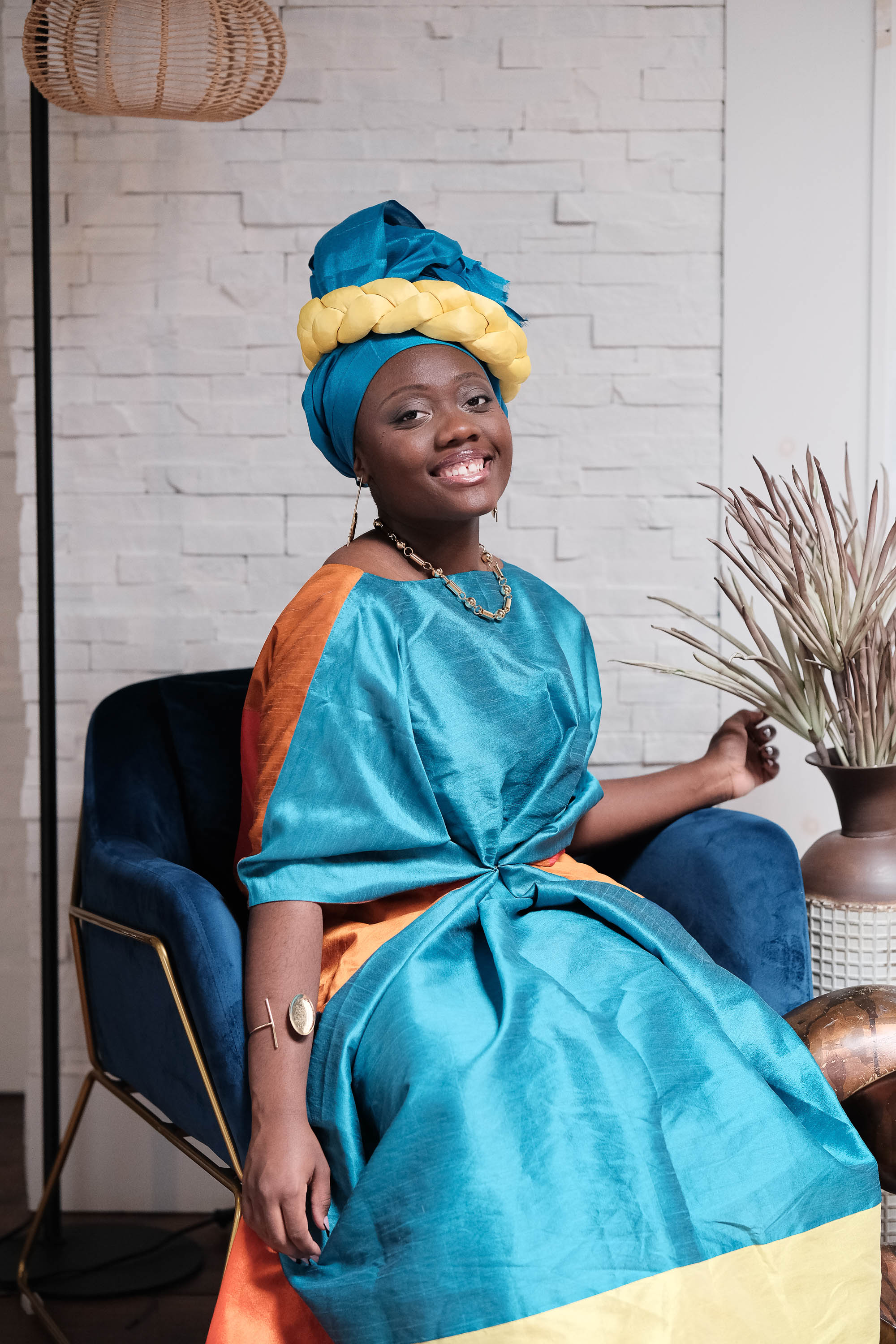 Marie-Paul seated in a blue velvet chair in vibrant teal and orange attire