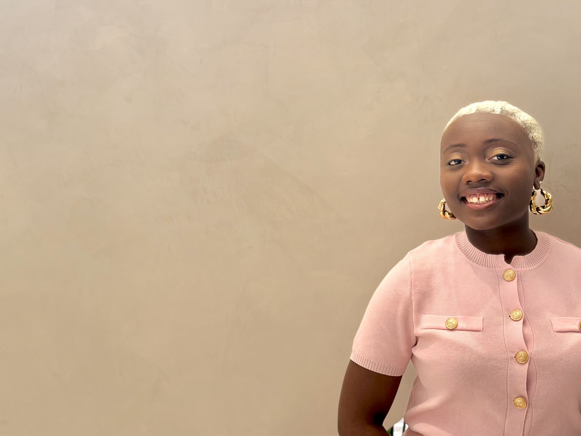 Marie-Paul smiling in a pink cardigan and gold earrings
